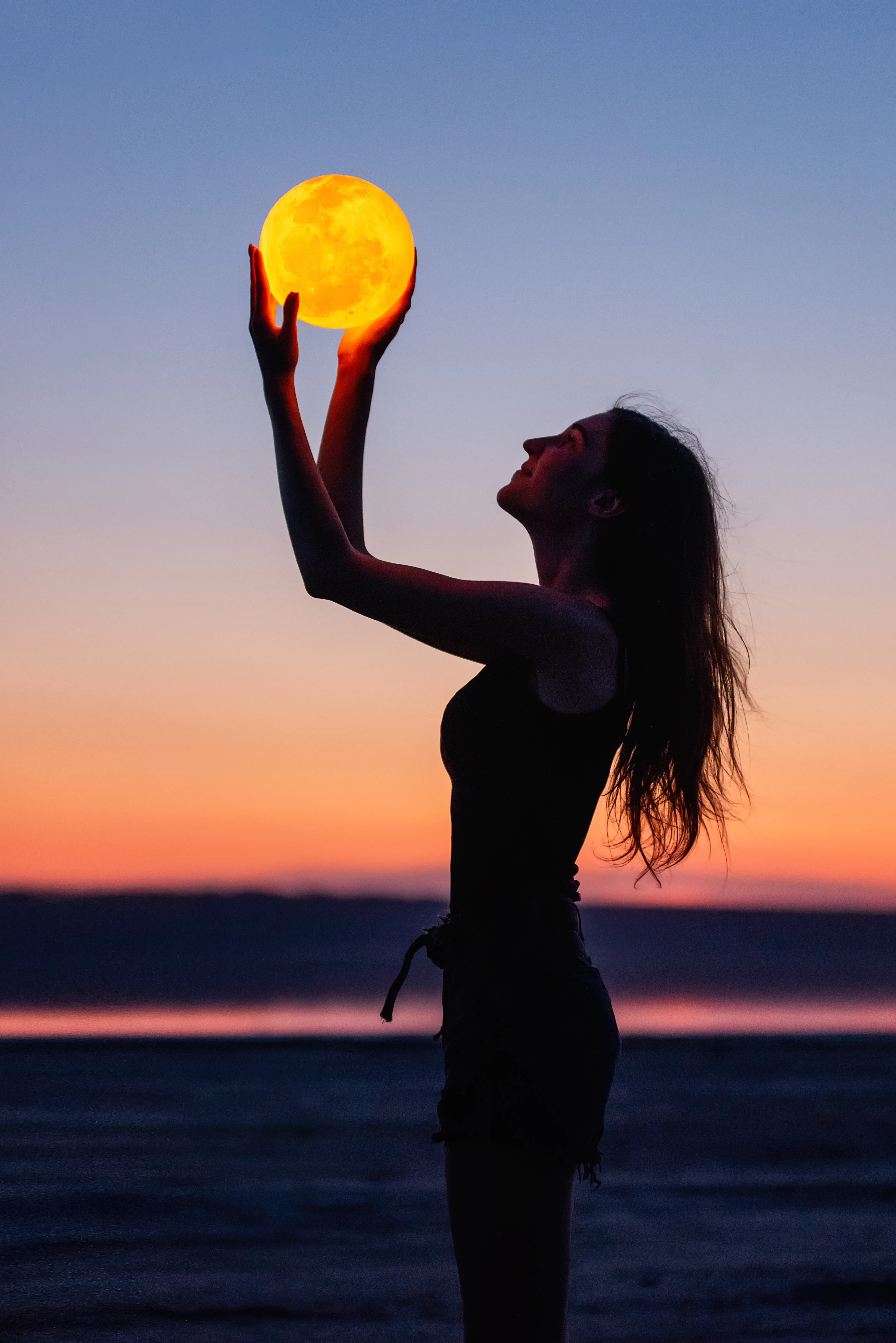 A young woman holds the full moon in her hands against the backdrop of a red sunset. Millennial blogger leads social media. Girl silhouette portrait. Astrology, Waxing Crescent. Copy space